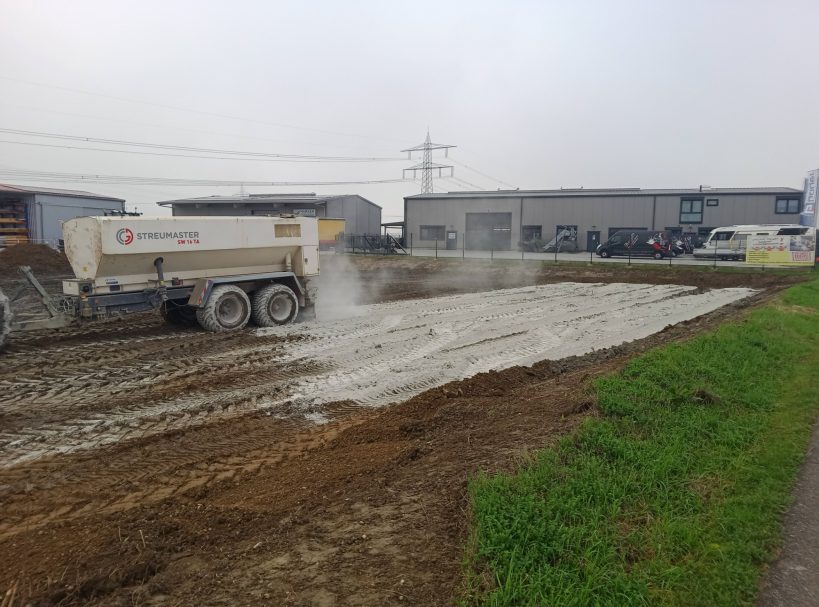 Baustelle mit einem Lkw, der frischen Beton auf eine unebene Fläche verteilt.