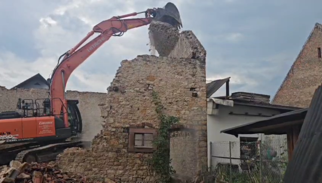 Ein Bagger reißt eine teilweise abgerissene Steinmauer in einem Gebäude ab.