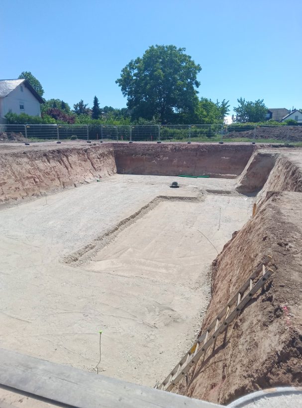 Baustelle mit ausgehobenem Erdreich für ein Fundament unter strahlend blauem Himmel.
