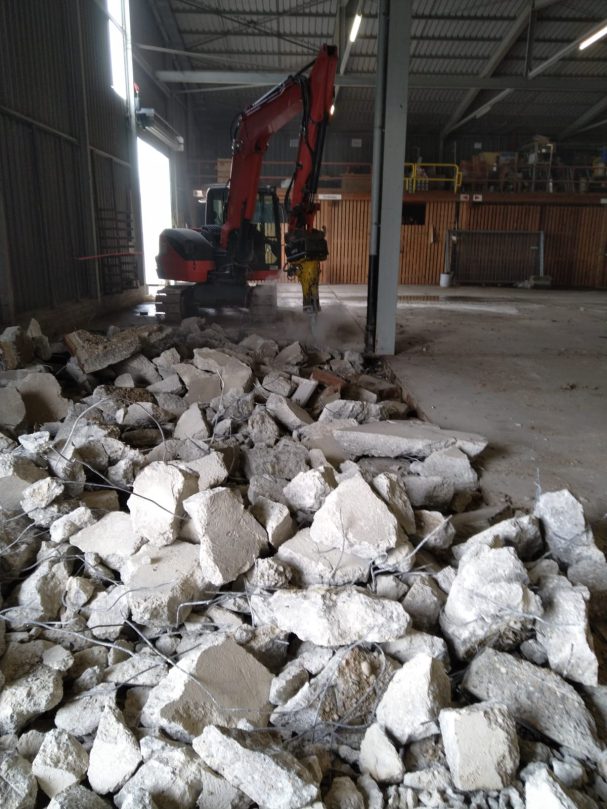 Bauschutt liegt auf dem Boden, ein Bagger arbeitet im Hintergrund.