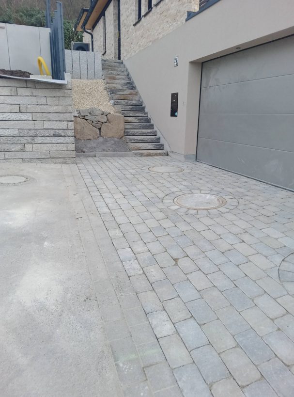 Verklinkerte Einfahrt mit Steinstufen und Garage, modernes Wohnhaus im Hintergrund.