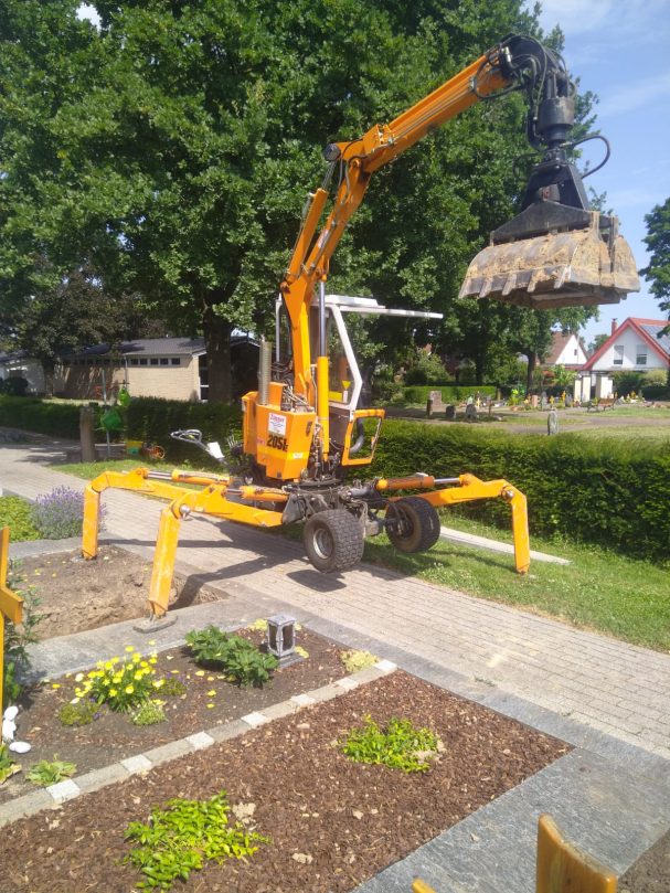 Gelber Bagger mit Greifarm hebt eine Last in einer Gartenlandschaft.