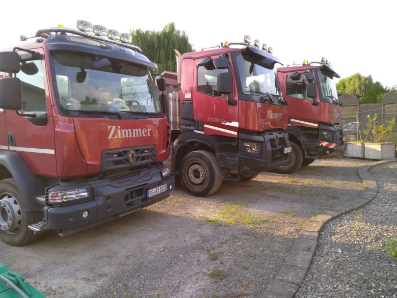 Drei rote Lkw parken nebeneinander auf einem Hof.