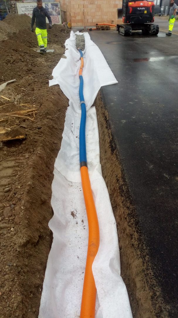 Graben mit einer blauen und einer orangefarbenen Leitung, umgeben von Erde.