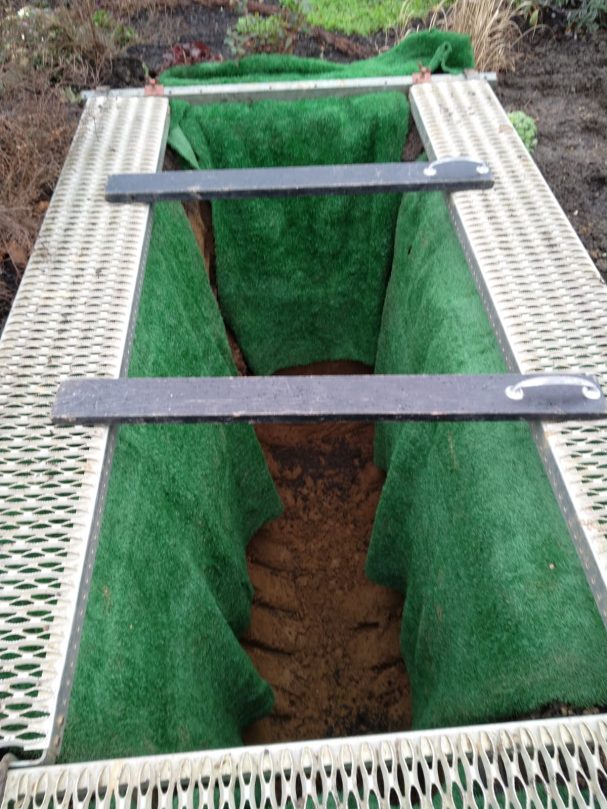 Offenes Grab mit grünem Samt ausgeschlagen und Holzabdeckungen.